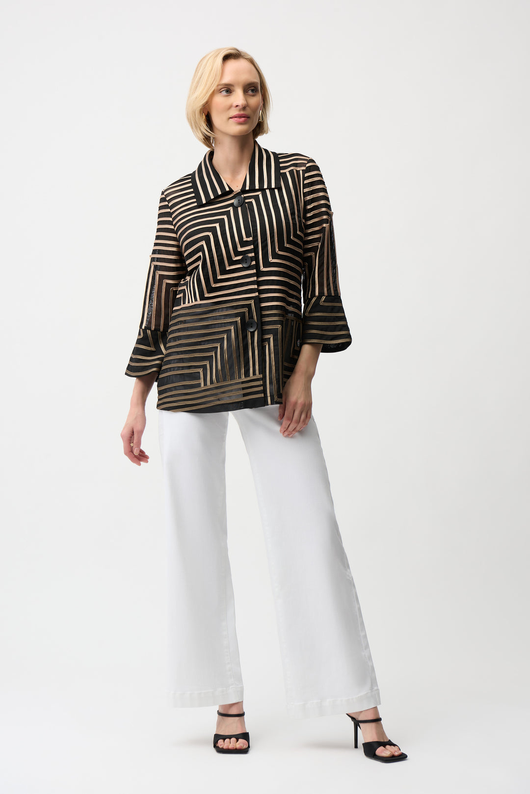 Woman wearing a black and gold patterned blouse with white pants on a white background