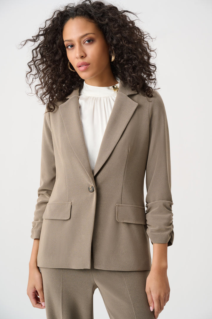 Woman wearing a taupe sports blazer with a white shirt on a plain background