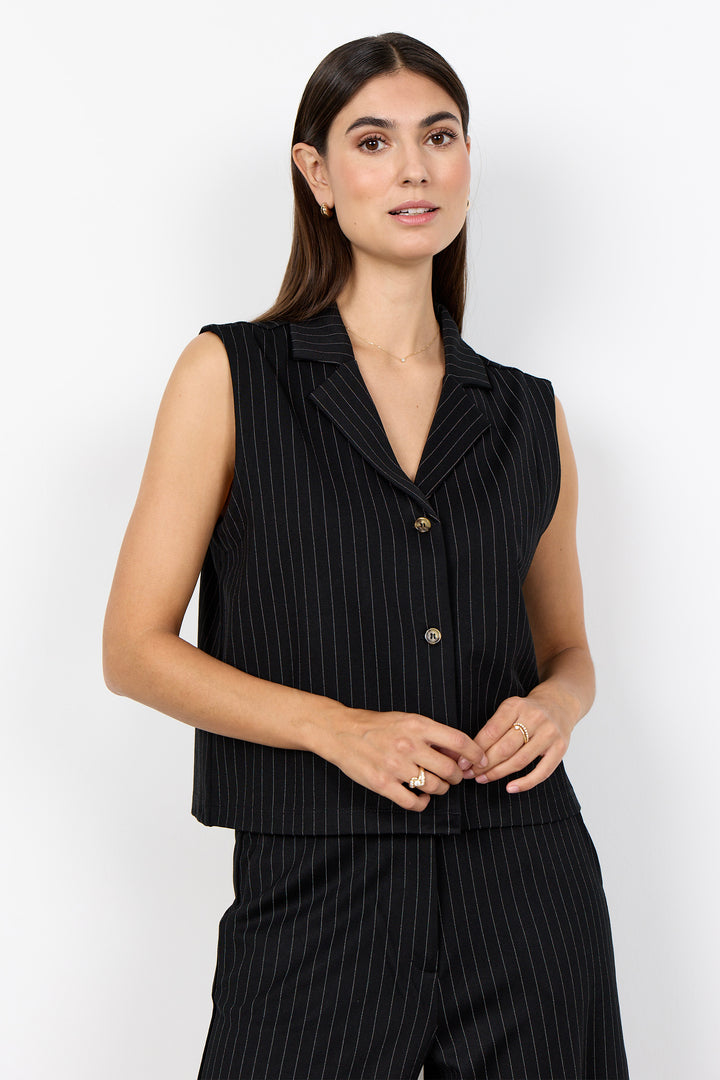 woman wearing a black pinstripe vest and matching pants on a  white background. 