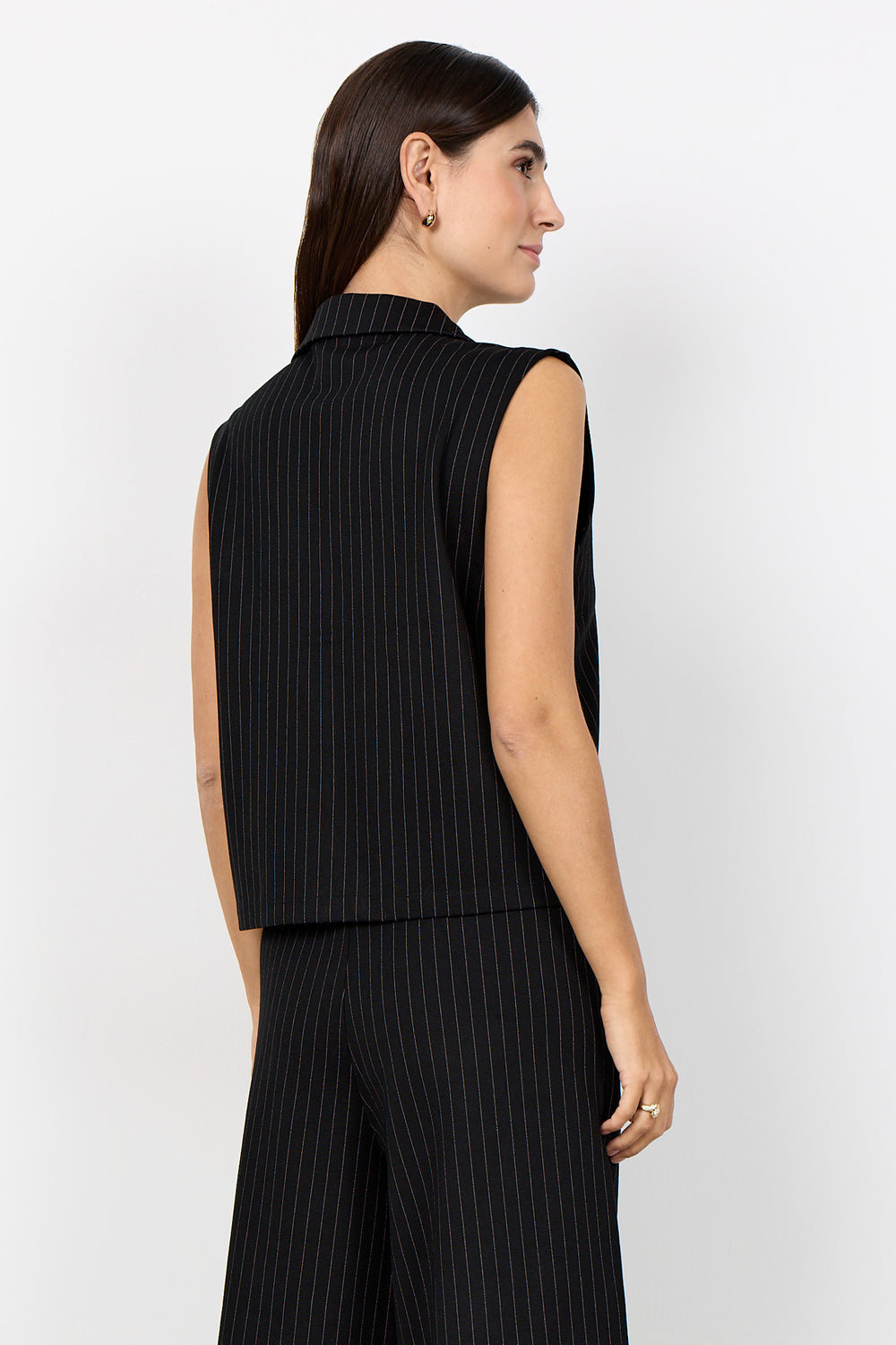 woman wearing a black pinstripe vest and matching pants on a  white background. 
