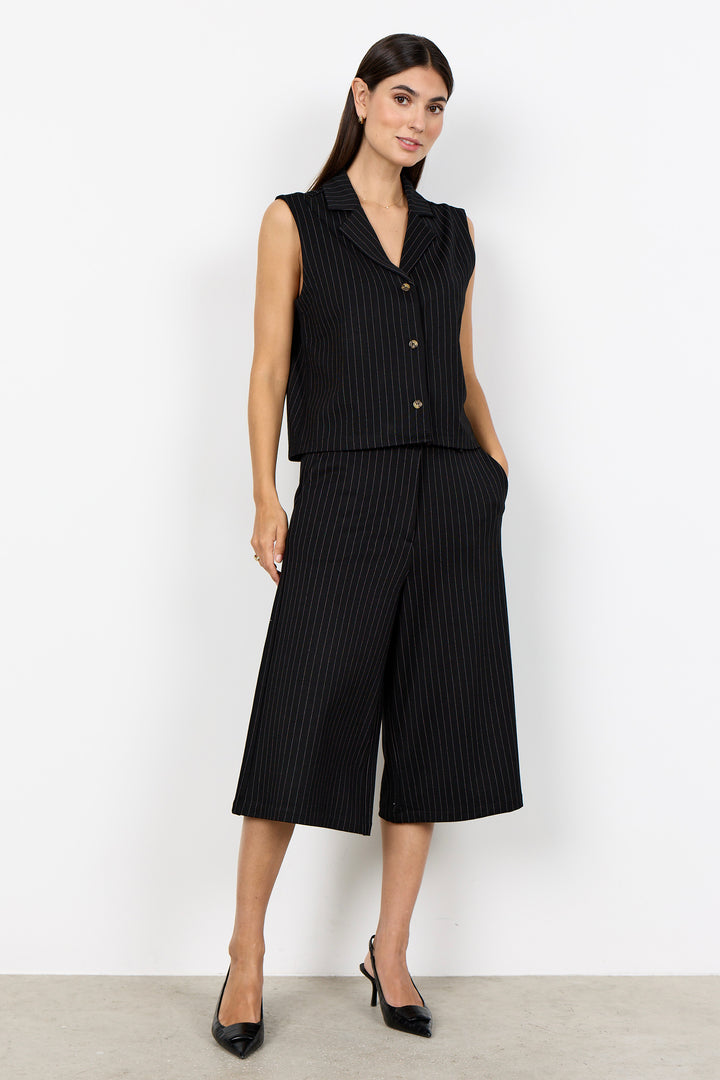 woman wearing a black pinstripe vest and matching pants on a  white background. 
