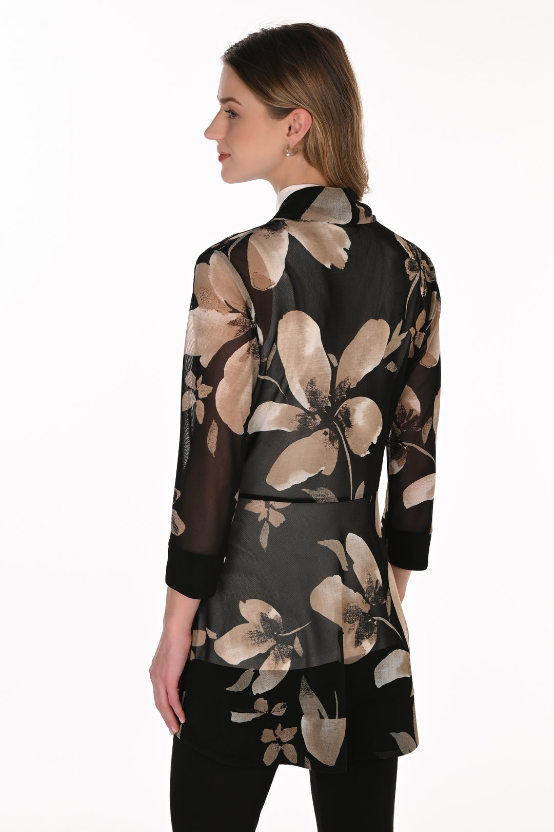 A woman shown from the back wearing a sheer black long-sleeve tunic top with a large beige floral print, paired with black pants, against a plain white background.