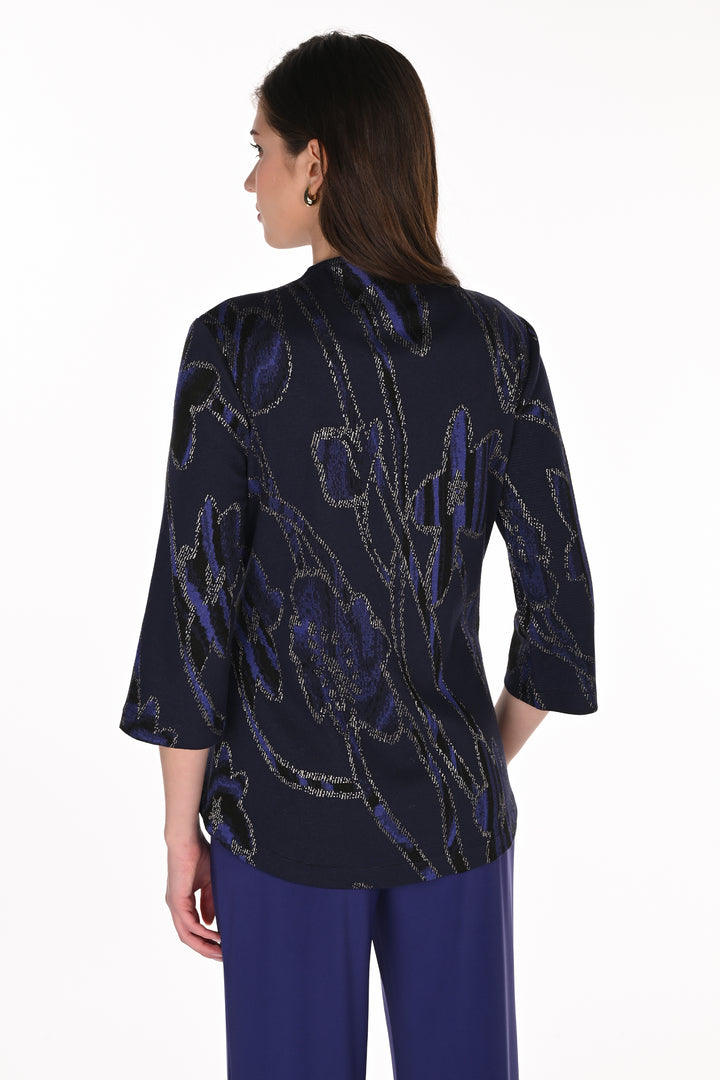 A woman shown from the back wearing a dark navy blue blouse with a purple and silver floral pattern, paired with solid purple trousers, against a plain white background.