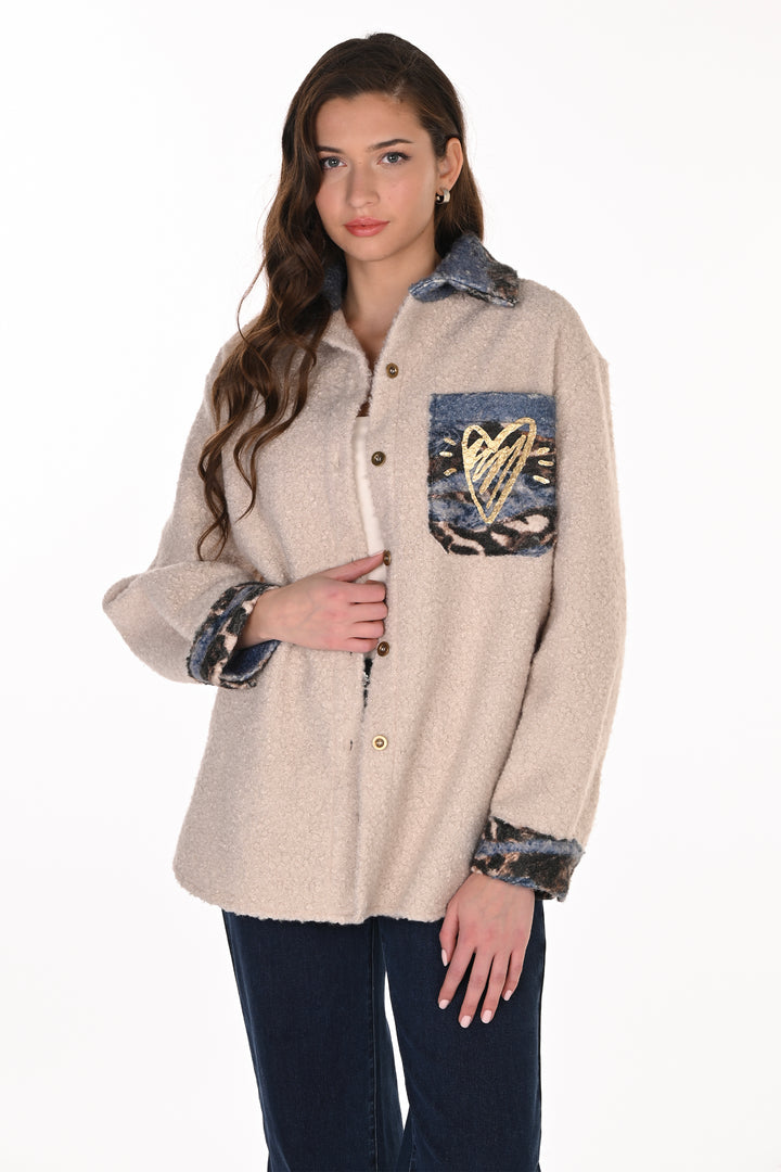 A woman shown from the back wearing a cream-colored fuzzy cardigan with a large graphic print featuring a stylized face, floral elements, and leopard print details, paired with dark blue jeans against a white background.