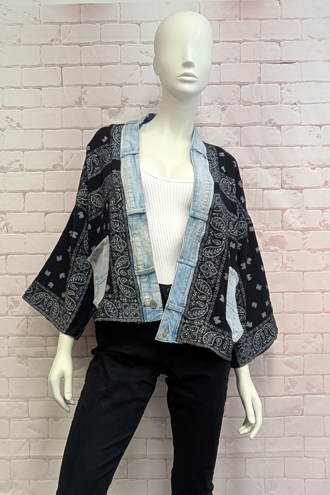 A black and light blue denim patchwork kimono jacket with paisley bandana patterns, displayed on a white mannequin against a pink brick wall background.