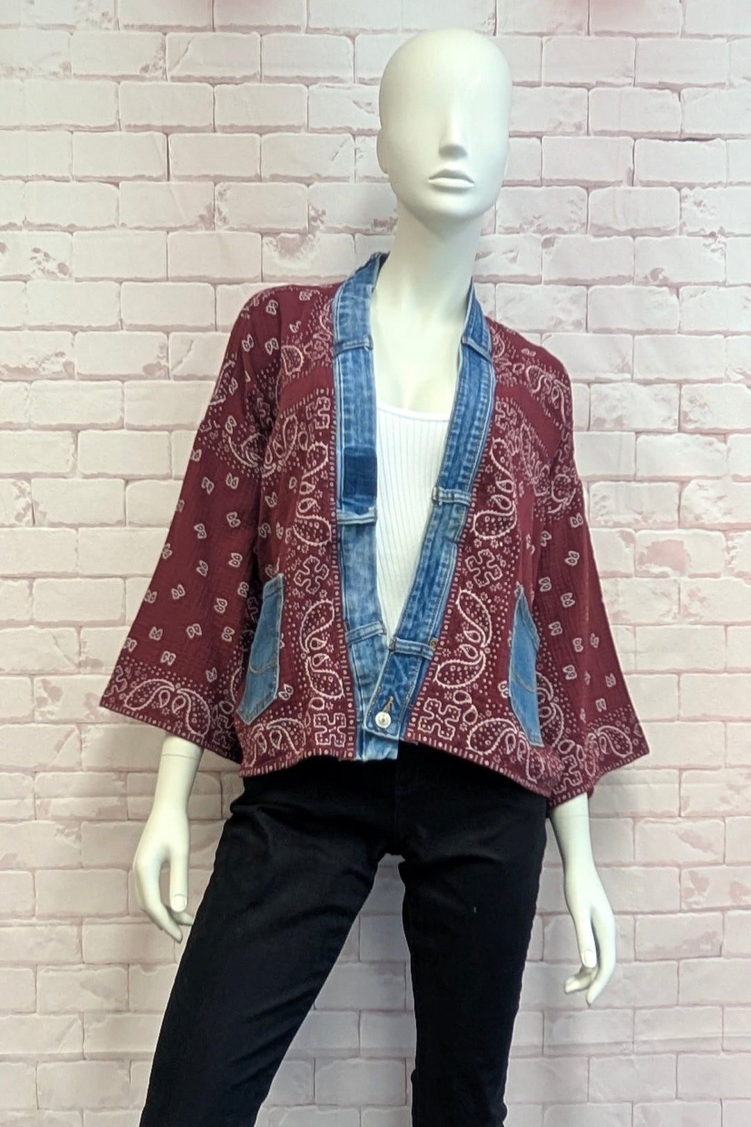 A mannequin wearing a cropped bandana jacket with denim trim over a white top and black pants, set against a light pink brick wall.