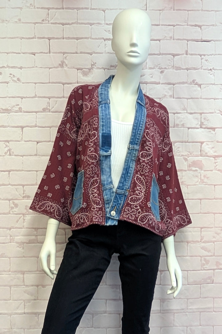 A mannequin wearing a cropped bandana jacket with denim trim over a white top and black pants, set against a light pink brick wall.