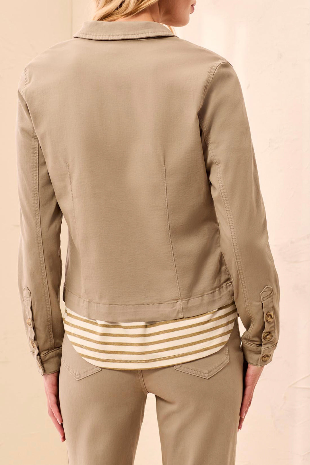 A woman shown from the back wearing a cropped tan utility jacket over a cream and tan striped shirt, paired with matching tan pants, against a light beige background.