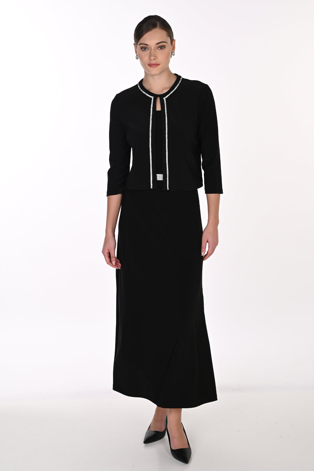 A woman modeling a black three-piece knit set consisting of a long-sleeve top with white trim, a matching midi skirt, and black pointed-toe heels, photographed against a plain white studio background.
