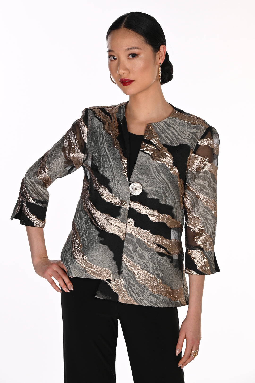 A woman modeling a three-quarter sleeve button-up jacket with a metallic marbled pattern in silver, bronze, and black, paired with black pants against a plain white background.