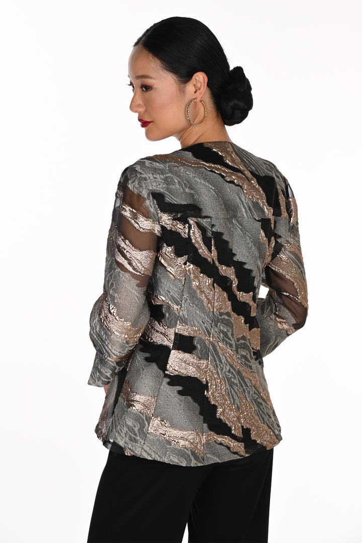 A woman shown from the back wearing a sheer long-sleeve blouse with an abstract metallic pattern in silver, bronze, and black, paired with black pants, against a plain white background.