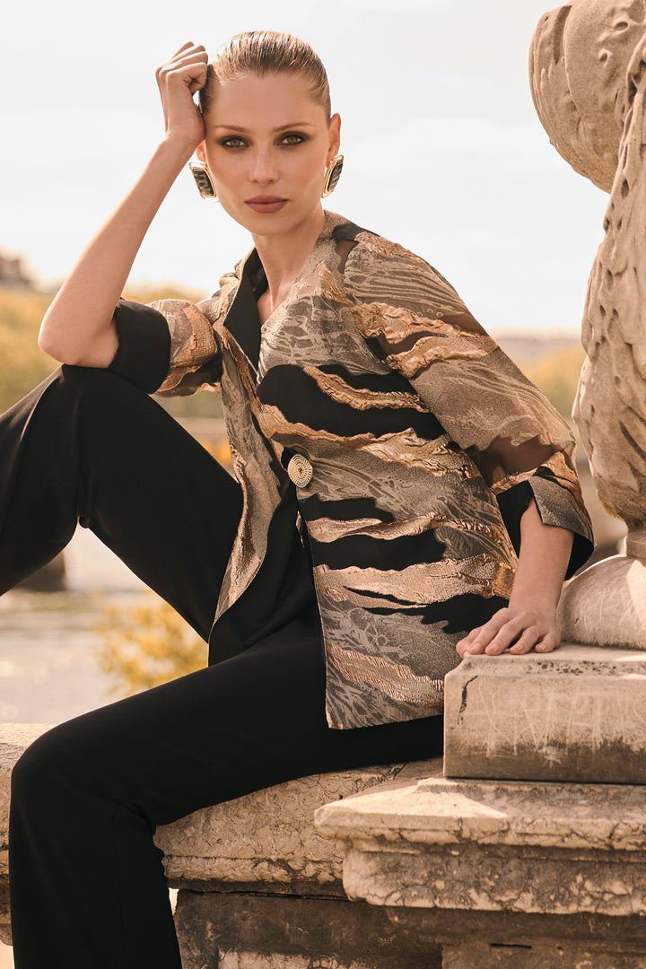 A woman models a patterned button-up shirt with black pants, sitting on stone steps outdoors.