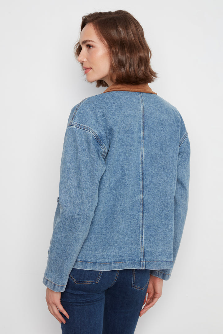A woman shown from the back wearing a light blue denim jacket with a brown collar, paired with dark blue jeans, against a plain white studio background.