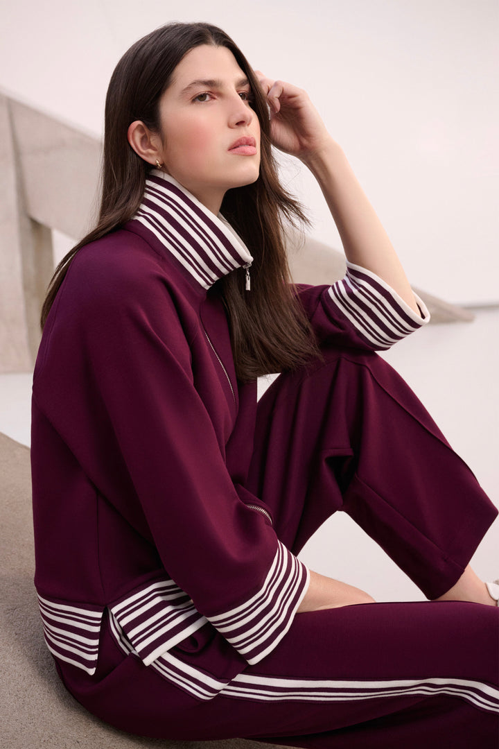 A woman wearing a matching burgundy lounge set with white and black striped trim, sitting on a modern concrete staircase.