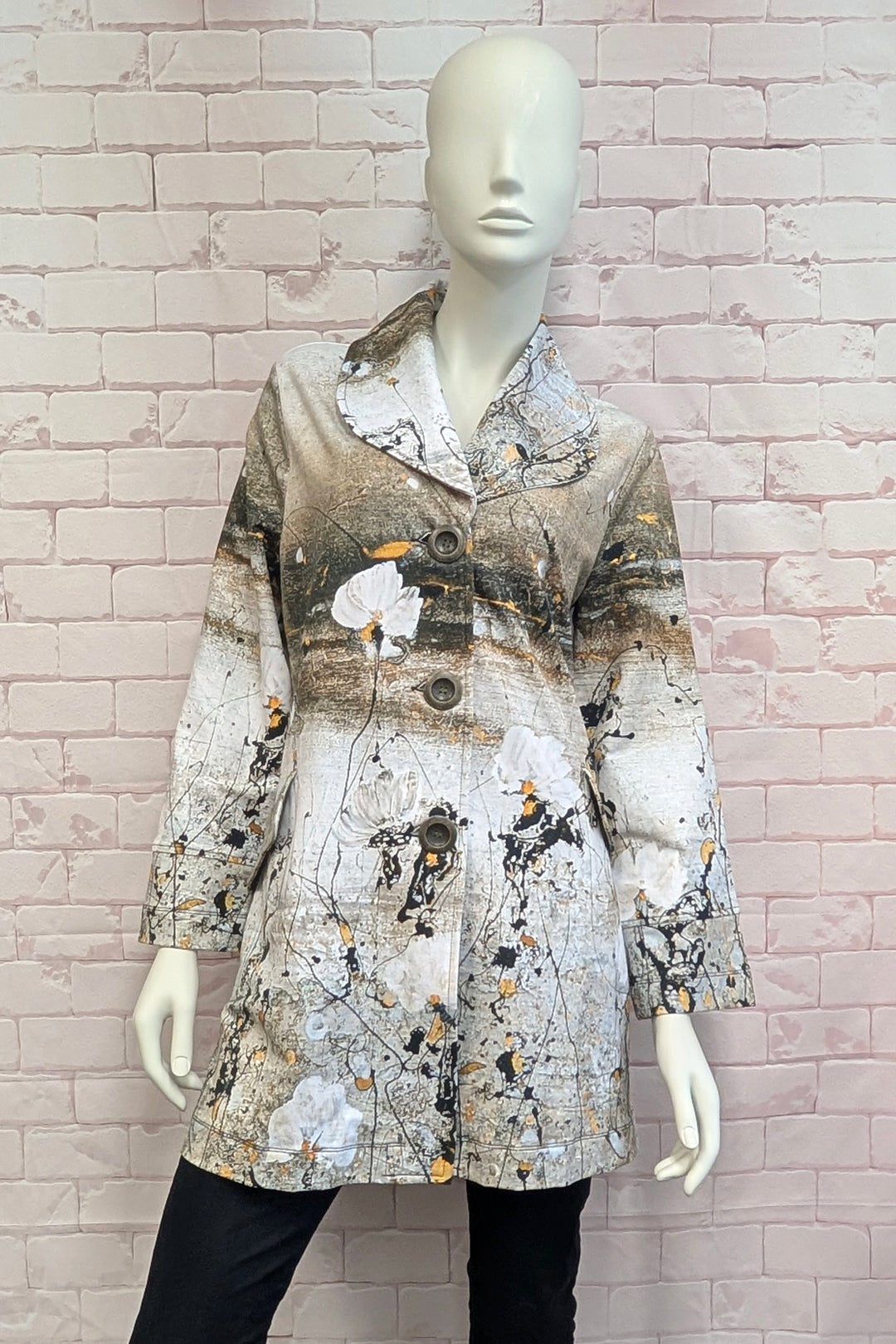 A women's long-sleeve coat with an abstract watercolor-style print in beige, brown, gray, black, and white, displayed on a female mannequin against a light pink brick wall.