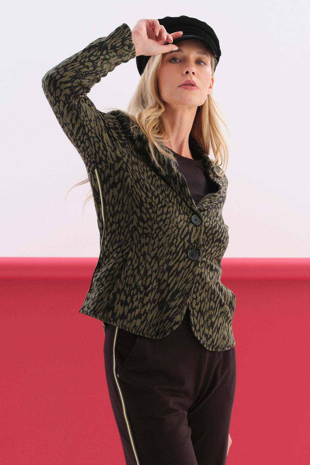 A woman modelling a long-sleeve blazer with a textured green and black abstract animal-print pattern against a plain white background.