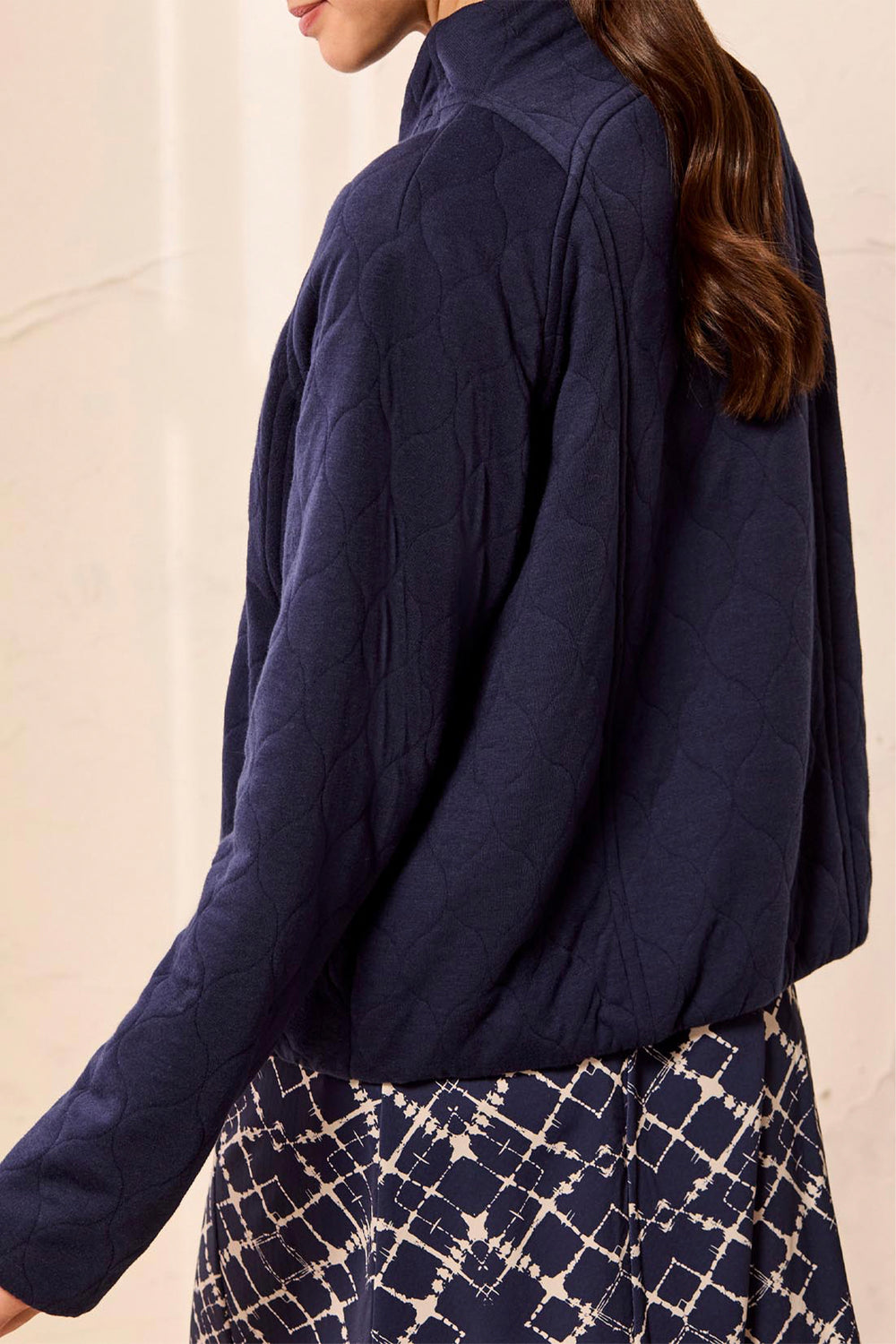 A woman wearing a navy blue quilted jacket, shown from a side-back angle against a light beige background.