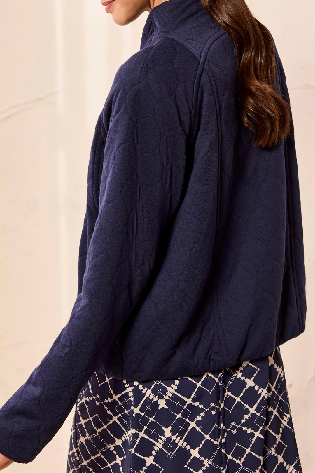A woman wearing a navy blue quilted jacket, shown from a side-back angle against a light beige background.