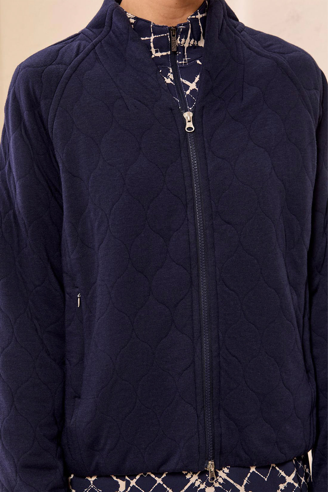 A close-up of a person wearing a navy blue quilted zip-up jacket over a patterned shirt and pants.