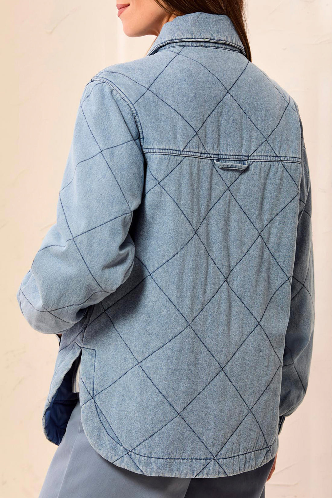 A person shown from the back wearing a light blue denim shirt jacket with a diamond quilted pattern on the back, paired with gray pants against a light beige background.