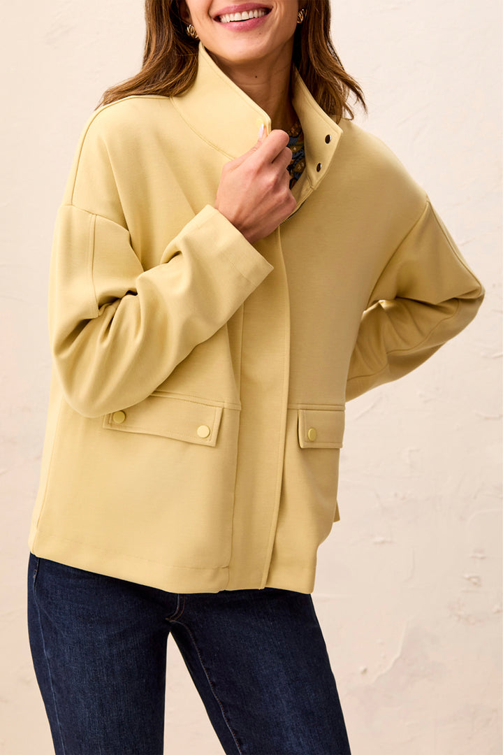 A woman wearing a pale yellow or butter-yellow jacket with a high stand collar, front button closure, and flap pockets with matching buttons.