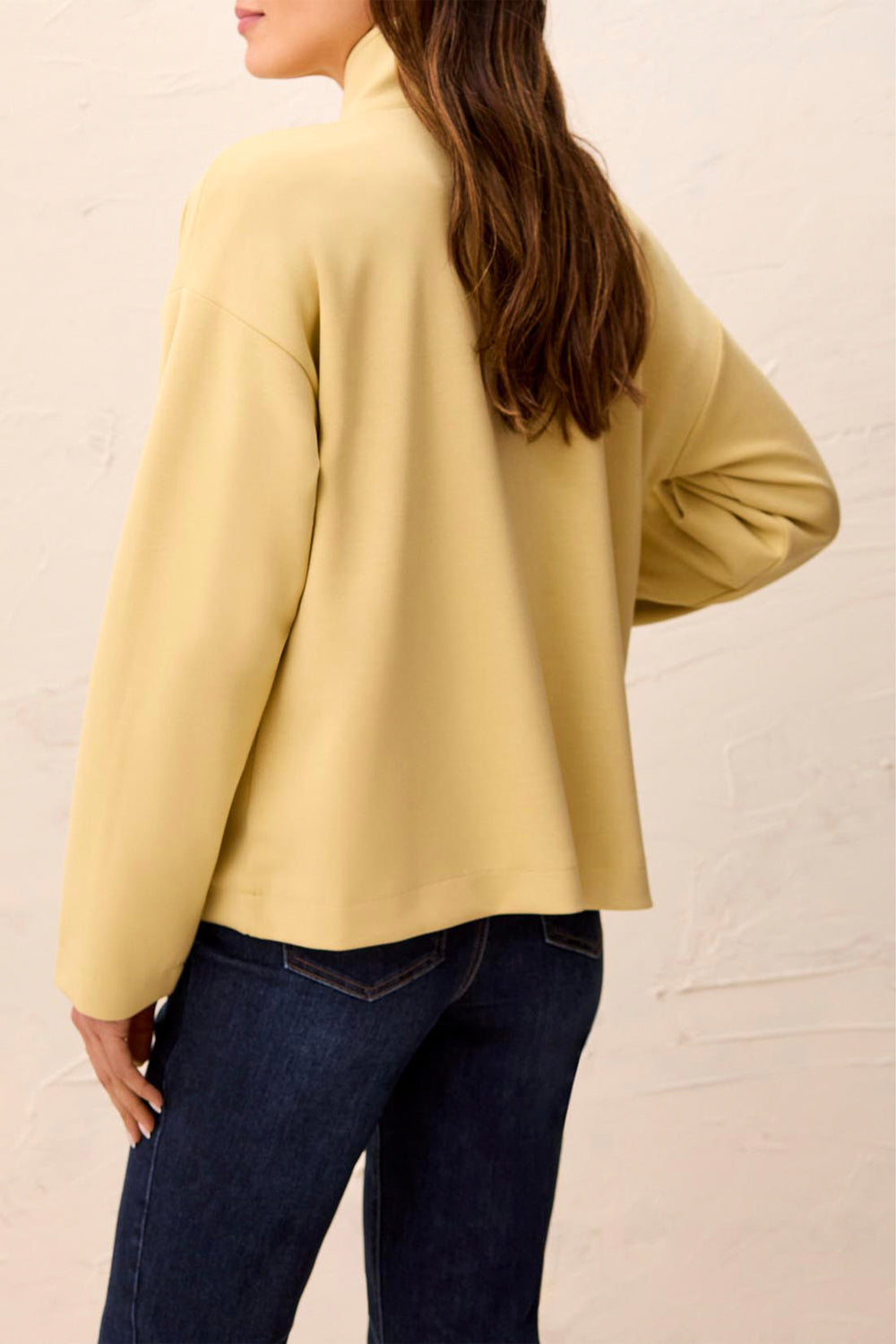 A woman shown from the back wearing a pale yellow or butter-yellow jacket with a high stand collar.