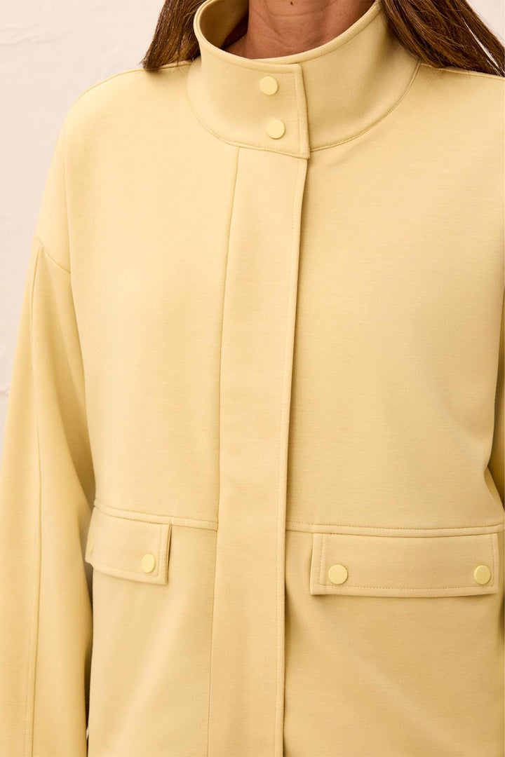 A close-up of a person wearing a pale yellow or butter-yellow jacket with a high stand collar, front button closure, and flap pockets with matching buttons.