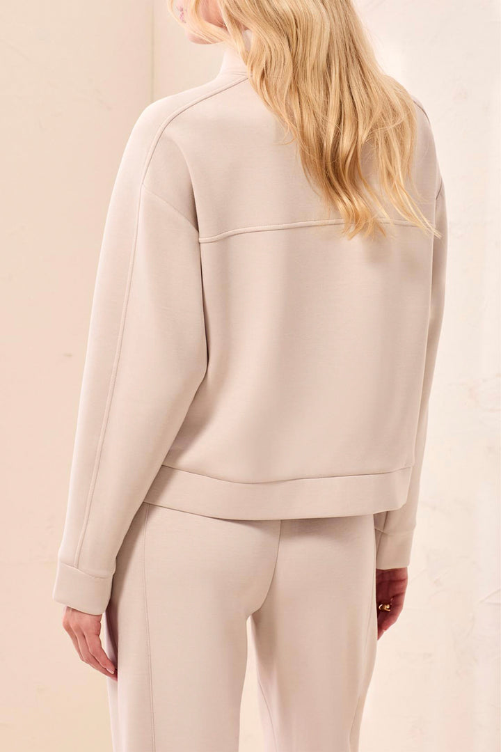 A woman shown from the back wearing a light beige cropped sweatshirt and matching sweatpants against a soft beige studio background.