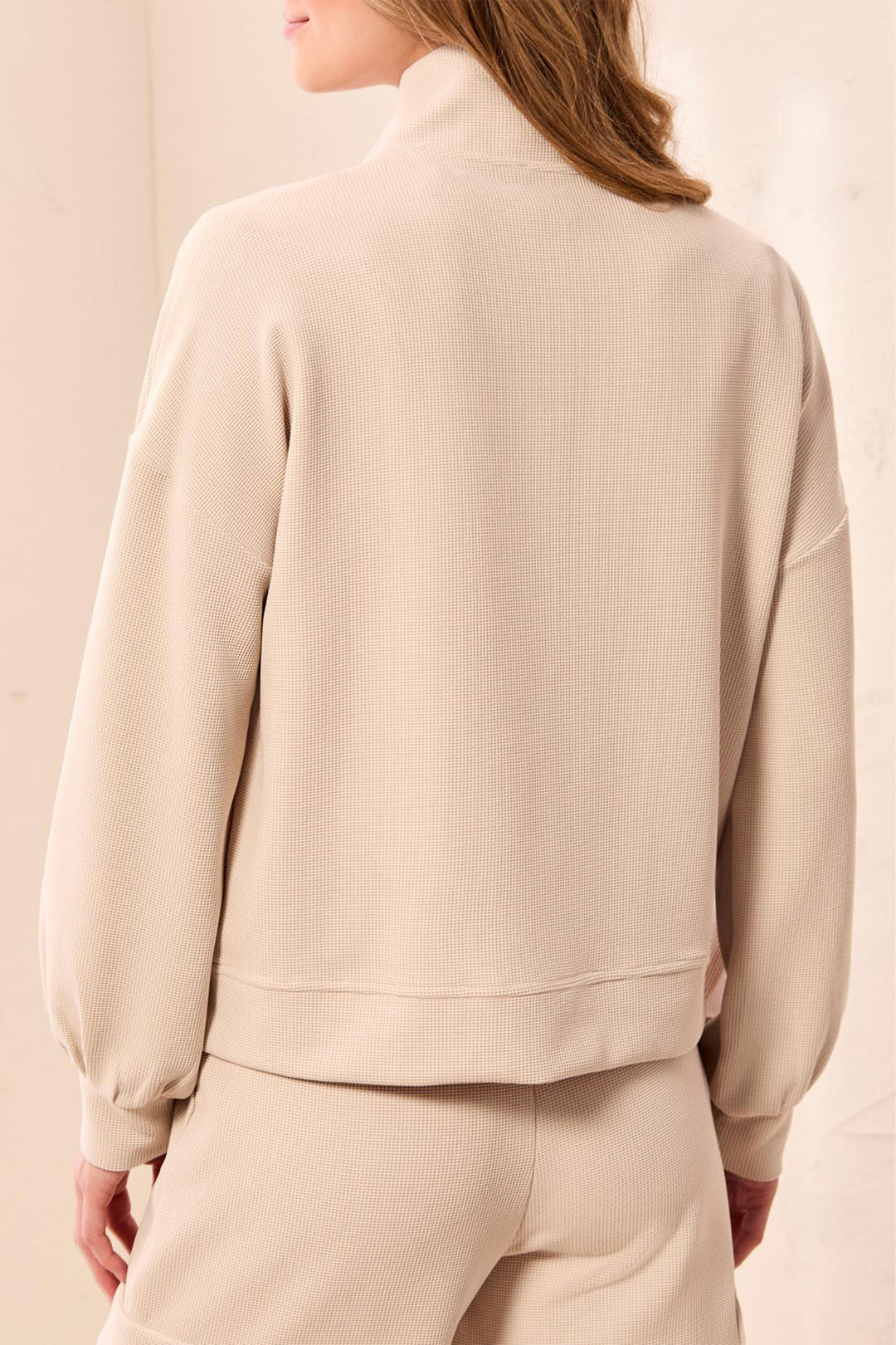 Person wearing a beige tracksuit against a plain background