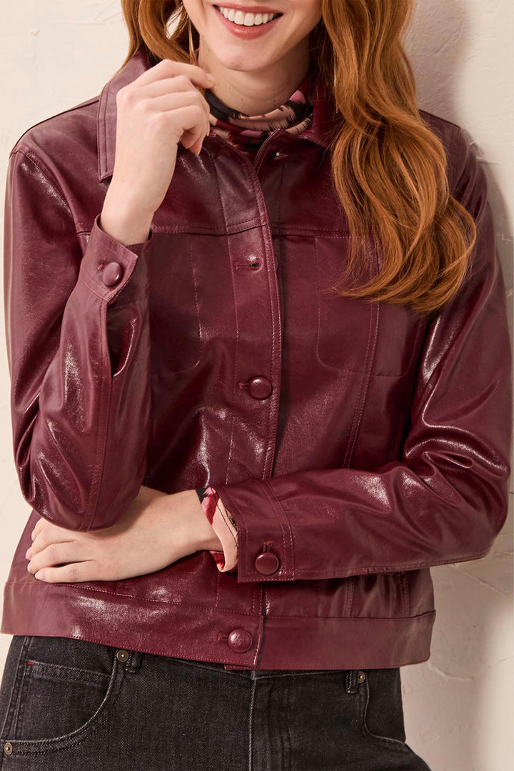 A woman wearing a cropped, glossy burgundy faux-leather jacket with snap buttons and a collar, paired with dark jeans.