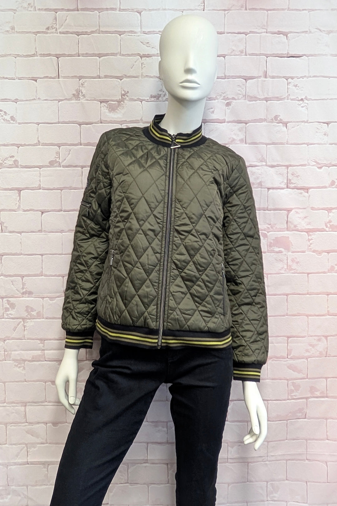 A mannequin wearing an olive green diamond-quilted bomber jacket with black and lime green striped ribbing on the collar, cuffs, and hem