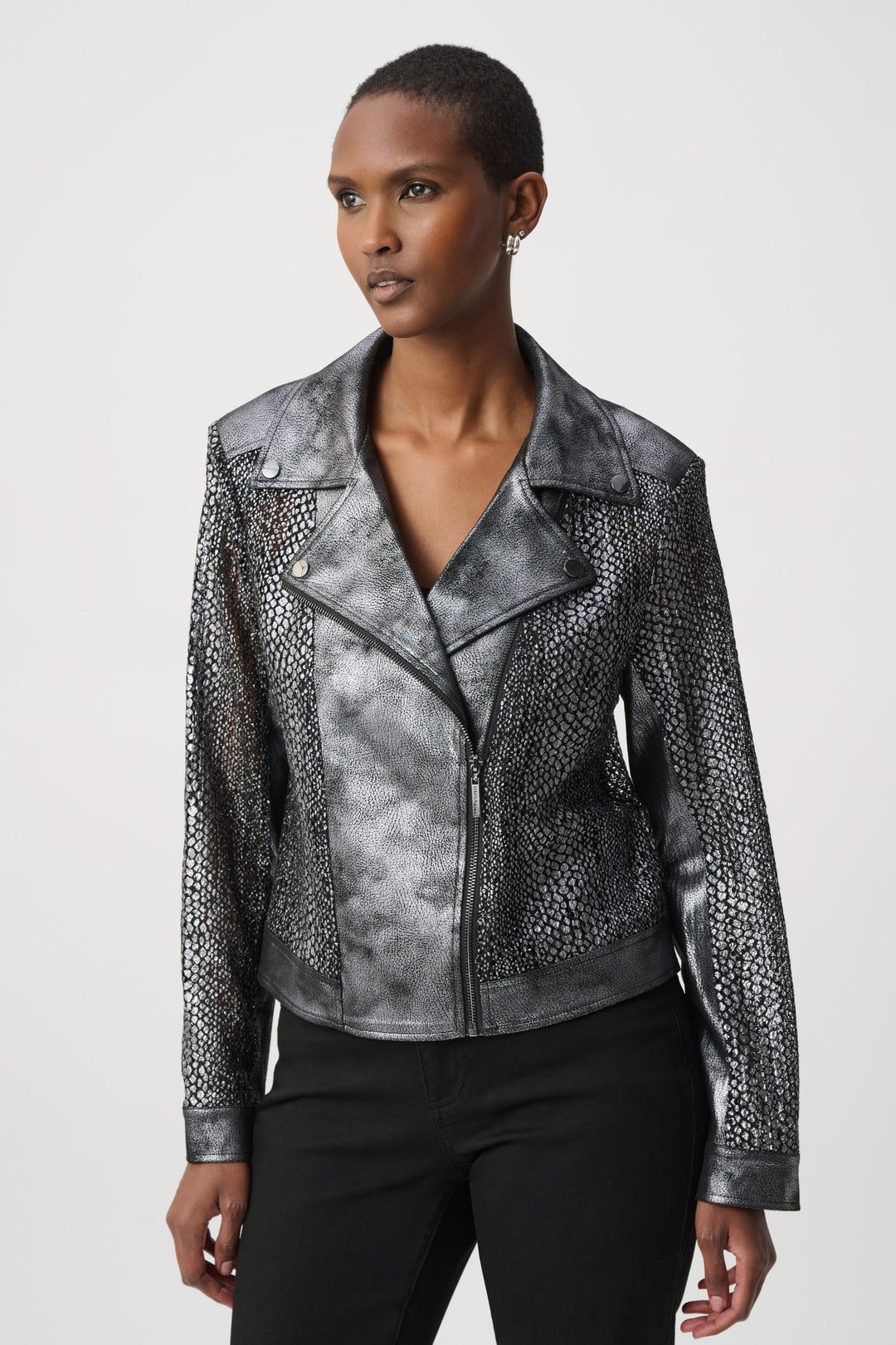 A woman wearing a dark silver moto style jacket, and black pants in front of a white background. 