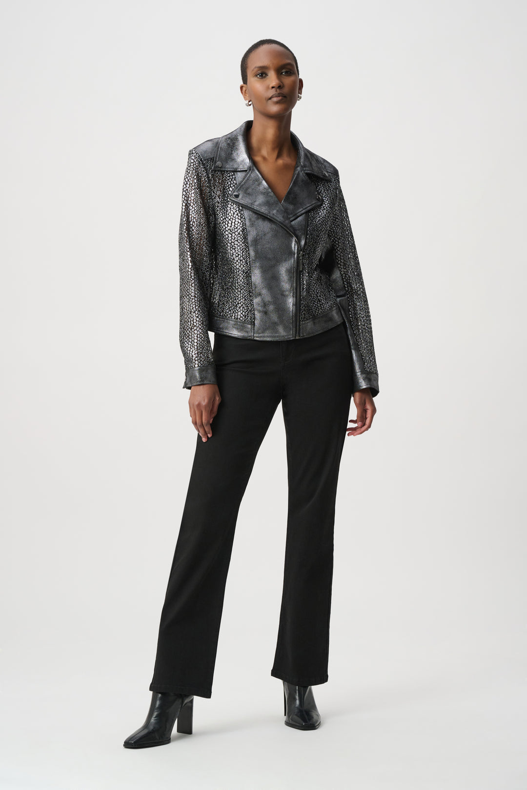 A woman wearing a dark silver moto style jacket, and black pants in front of a white background. 