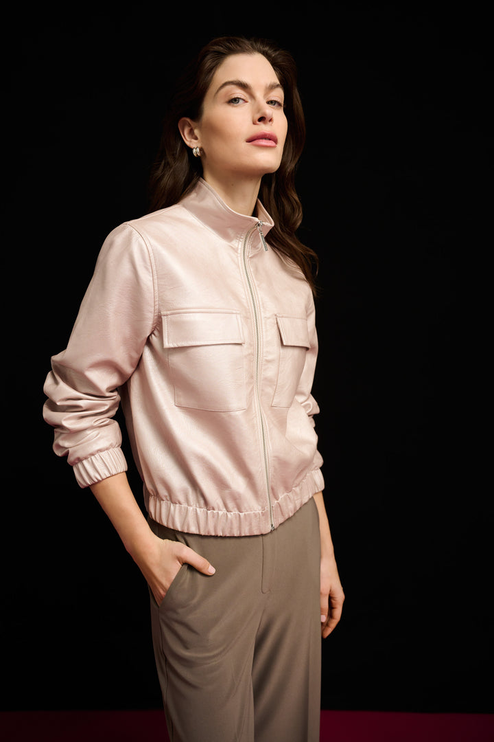 Woman wearing a light pink jacket and beige pants against a black background
