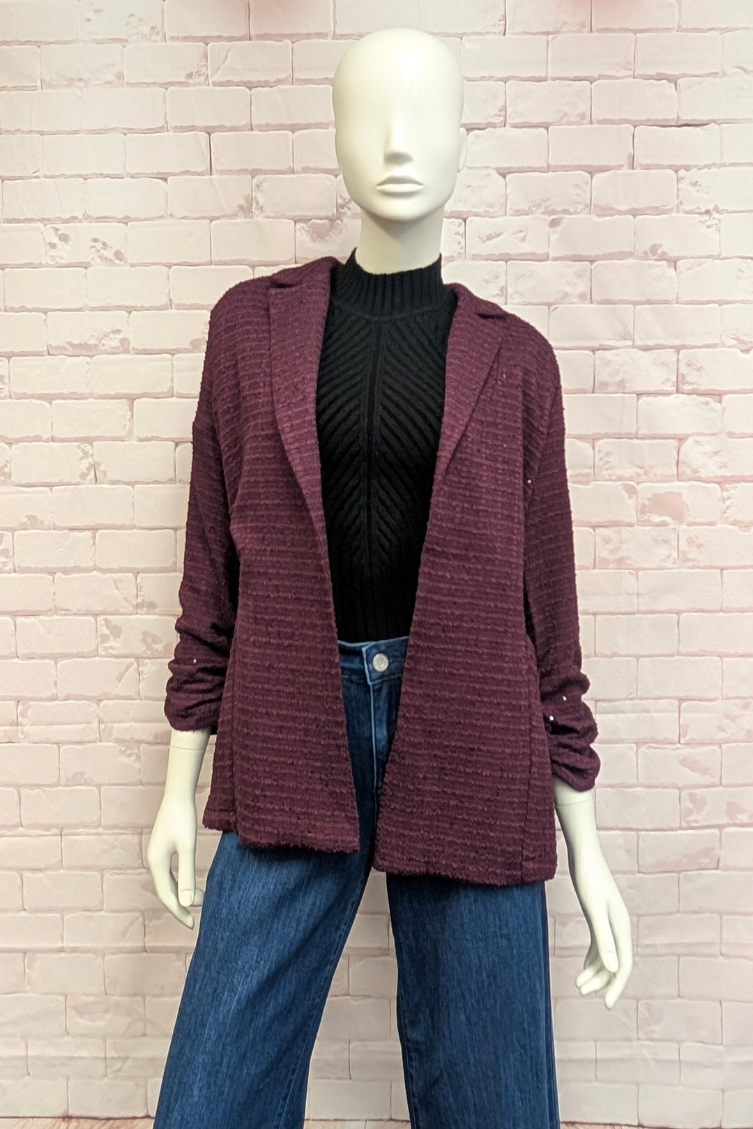 A mannequin in front of a brick wall modelling a burgundy boucle blazer with three-quarter sleeves.