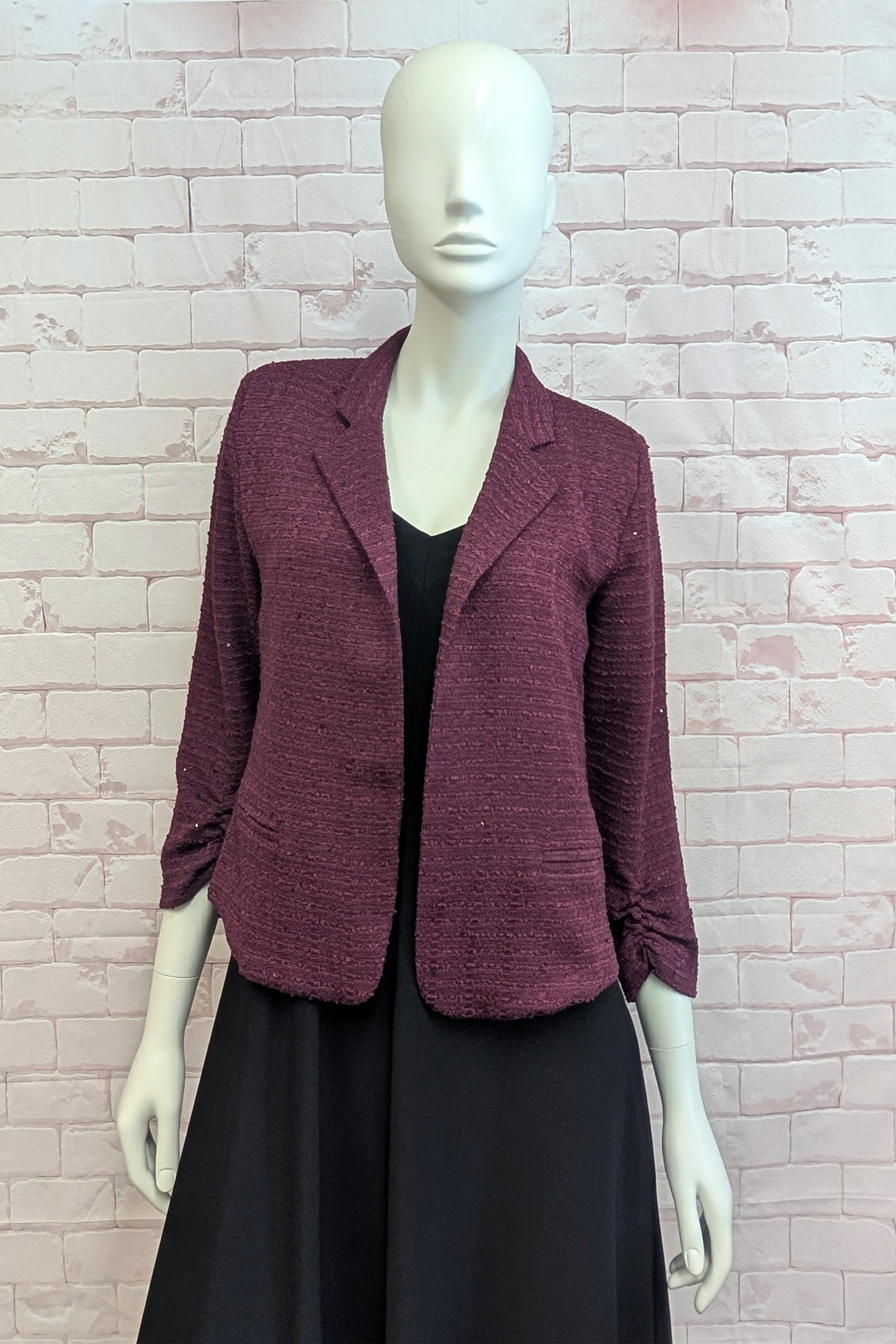 A mannequin wearing a burgundy blazer standing in front of a light brick wall. 