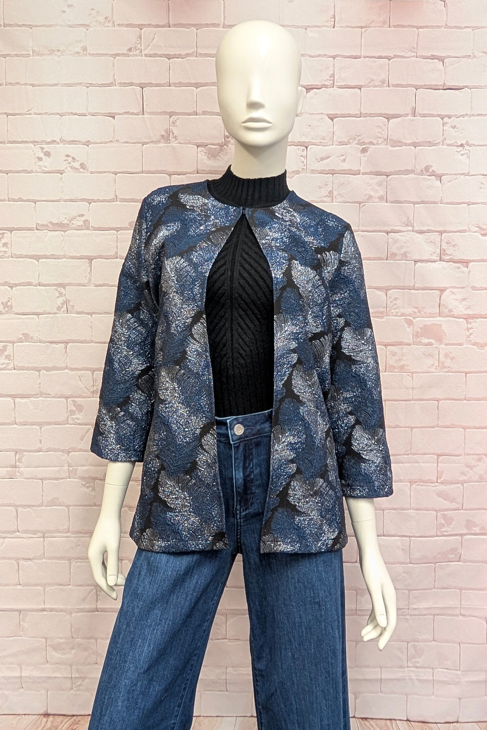 A mannequin standing in front of a brick background modelling a navy three-quarter sleeve jacket with a metallic feather print. 