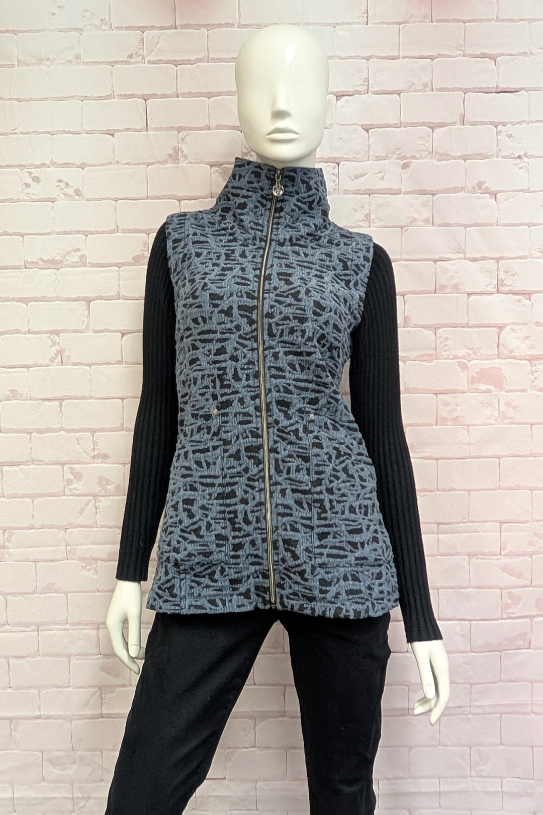 A female mannequin wearing a sleeveless zip-front vest with a high mock neck collar, featuring an abstract black and gray pattern.