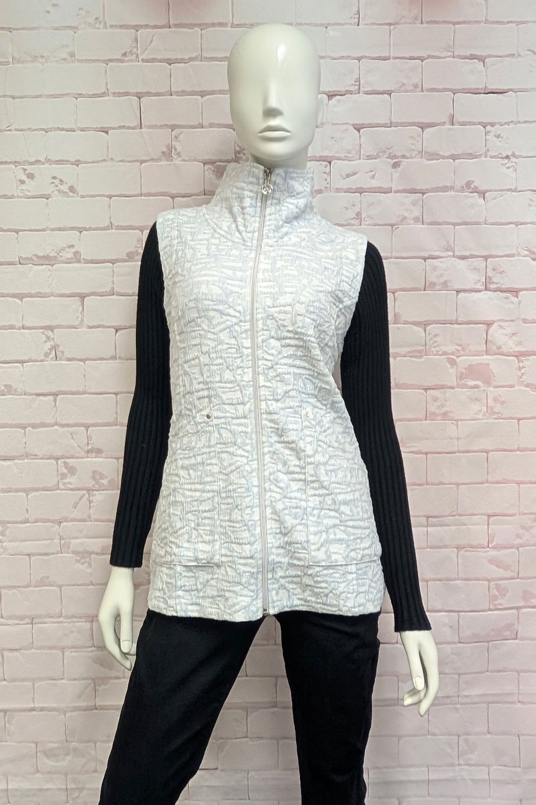 A female mannequin wearing a sleeveless zip-front vest with a high mock neck collar, featuring an abstract white and gray pattern.