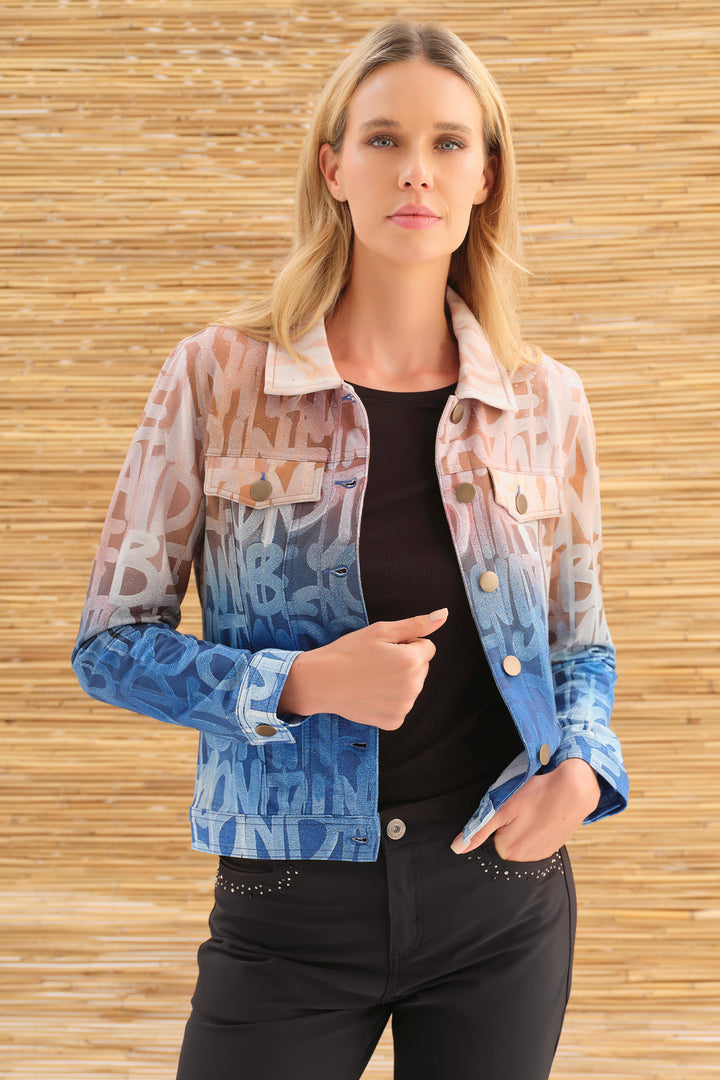 A woman modeling a cropped denim jacket with a blue-to-pink gradient and abstract lettering print, worn over a black top and black pants, set against a light wood slat wall background.
