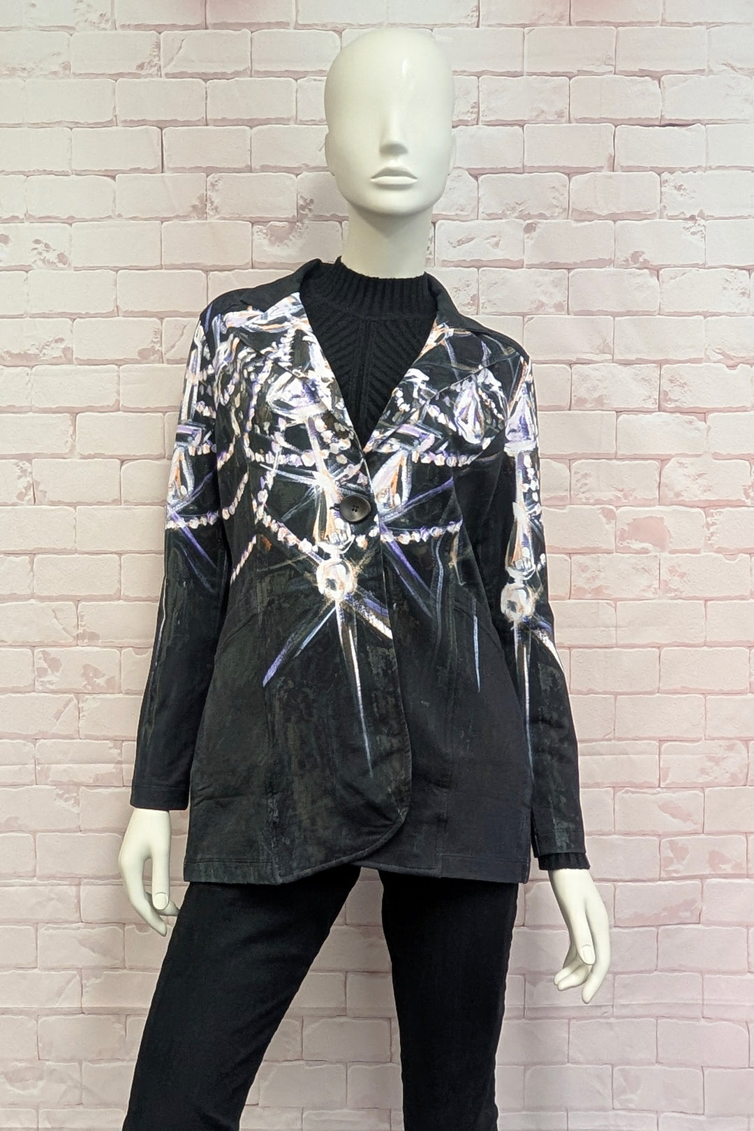 A black long-sleeve blazer with a silver and white metallic web-like pattern, displayed on a white mannequin against a light pink brick wall.