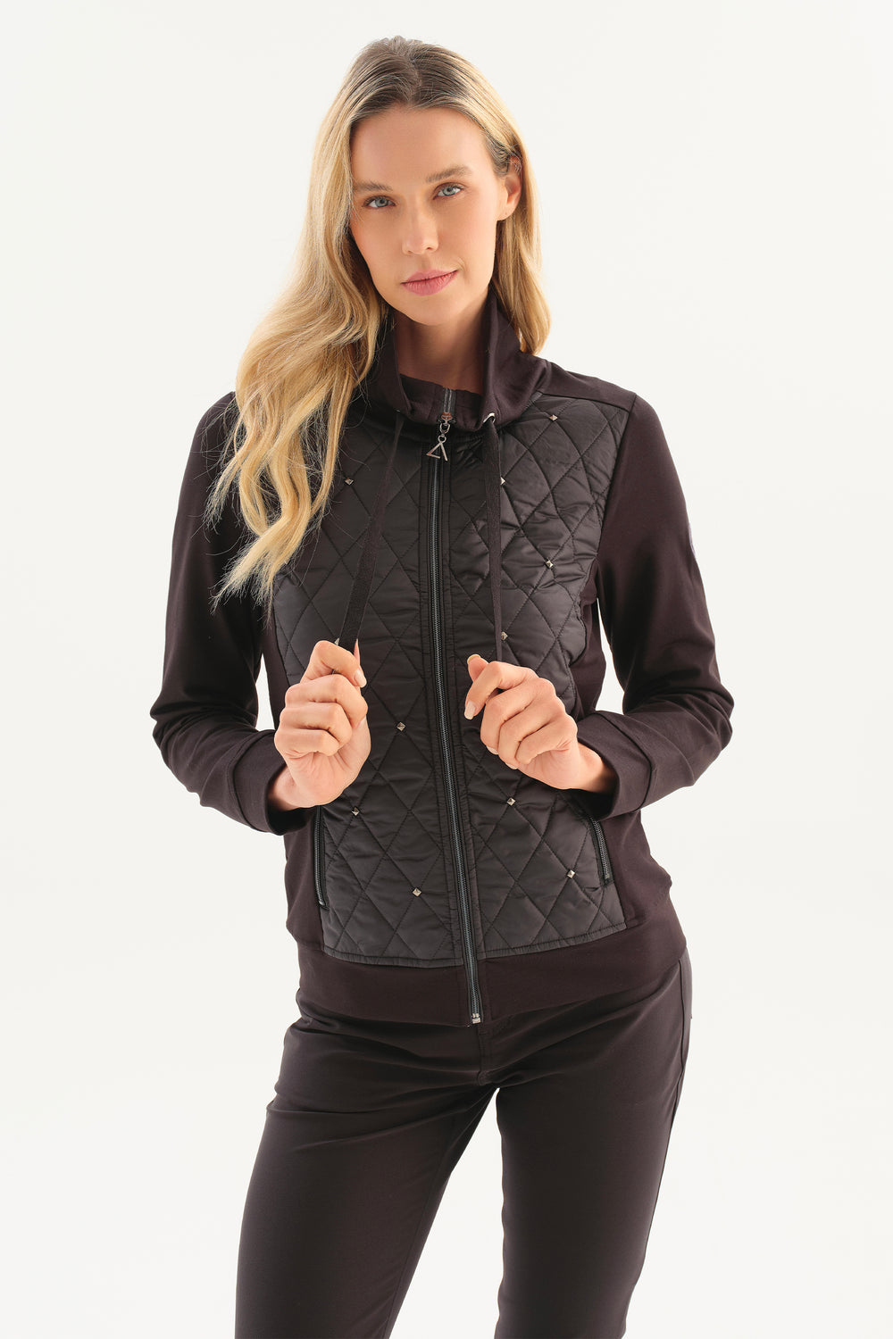 A woman modeling a dark brown and black quilted zip-front jacket with matching dark pants against a clean white studio background.