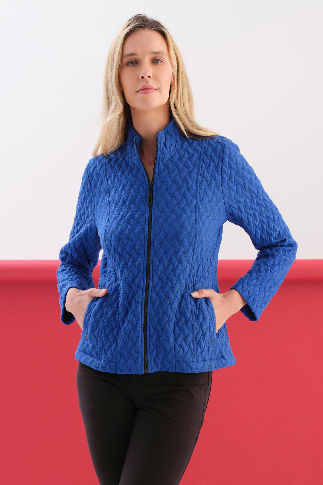 A women modelling a blue quilted zip front jacket in front of a white and red background. 