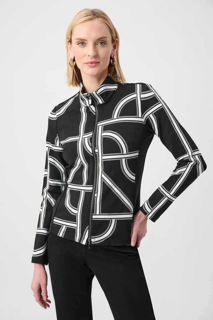 A woman standing in front of a light grey background wearing a black and white geometric print jacket and black pants. 