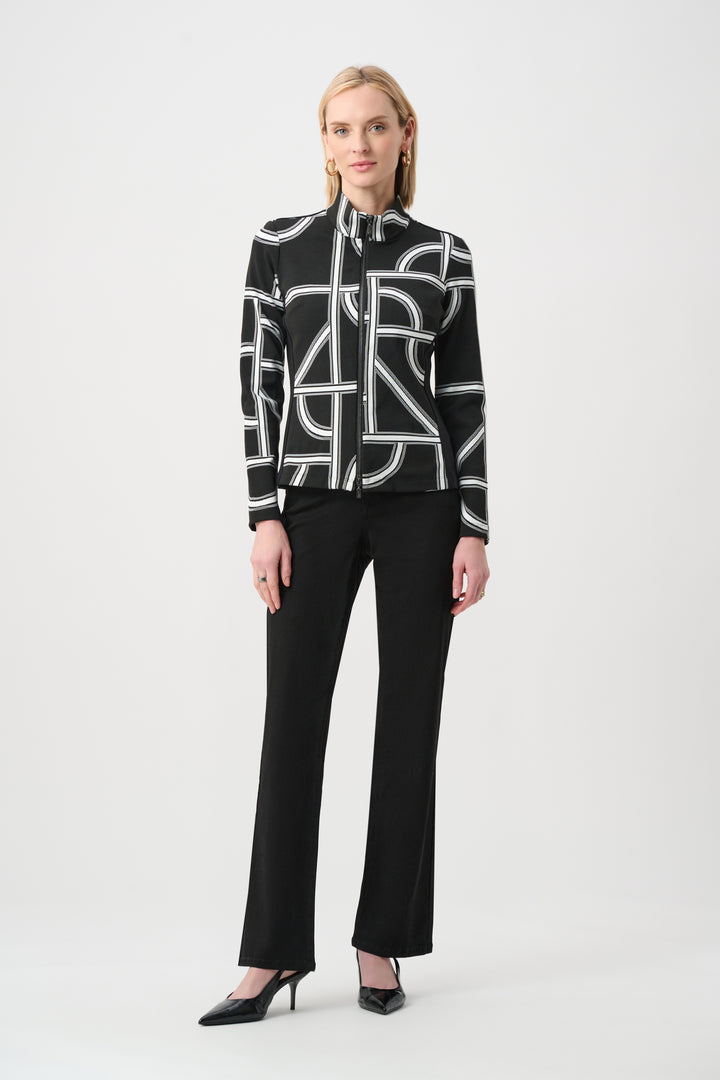 A woman standing in front of a light grey background wearing a black and white geometric print jacket and black pants. 