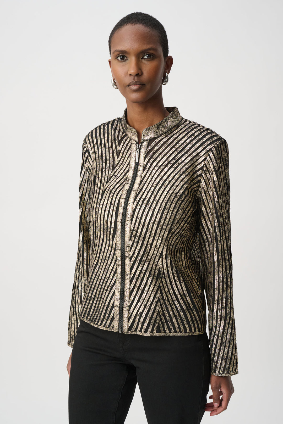 A woman standing in front of a light grey background wearing a metallic gold jacket and black pants. 