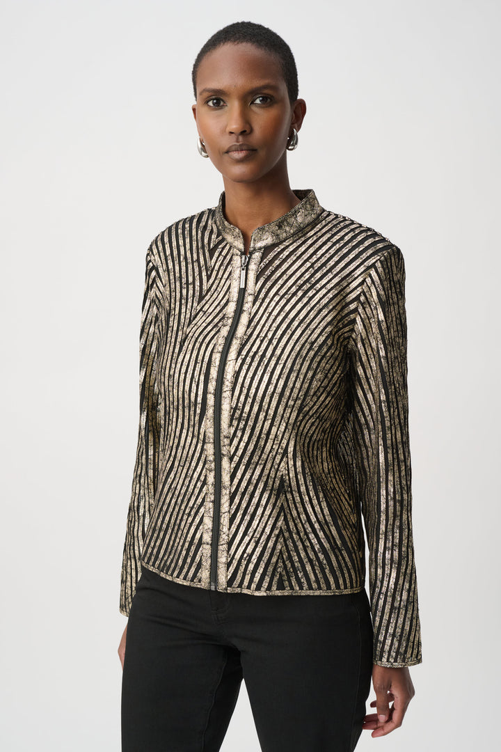 A woman standing in front of a light grey background wearing a metallic gold jacket and black pants. 