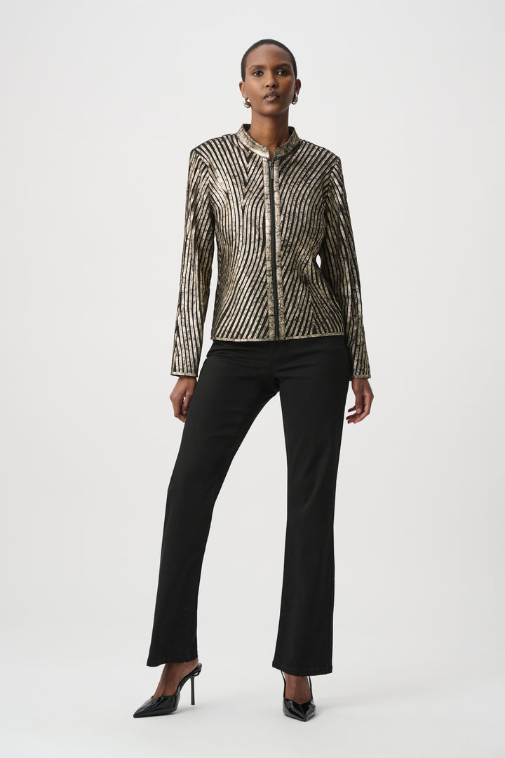 A woman standing in front of a light grey background wearing a metallic gold jacket and black pants. 