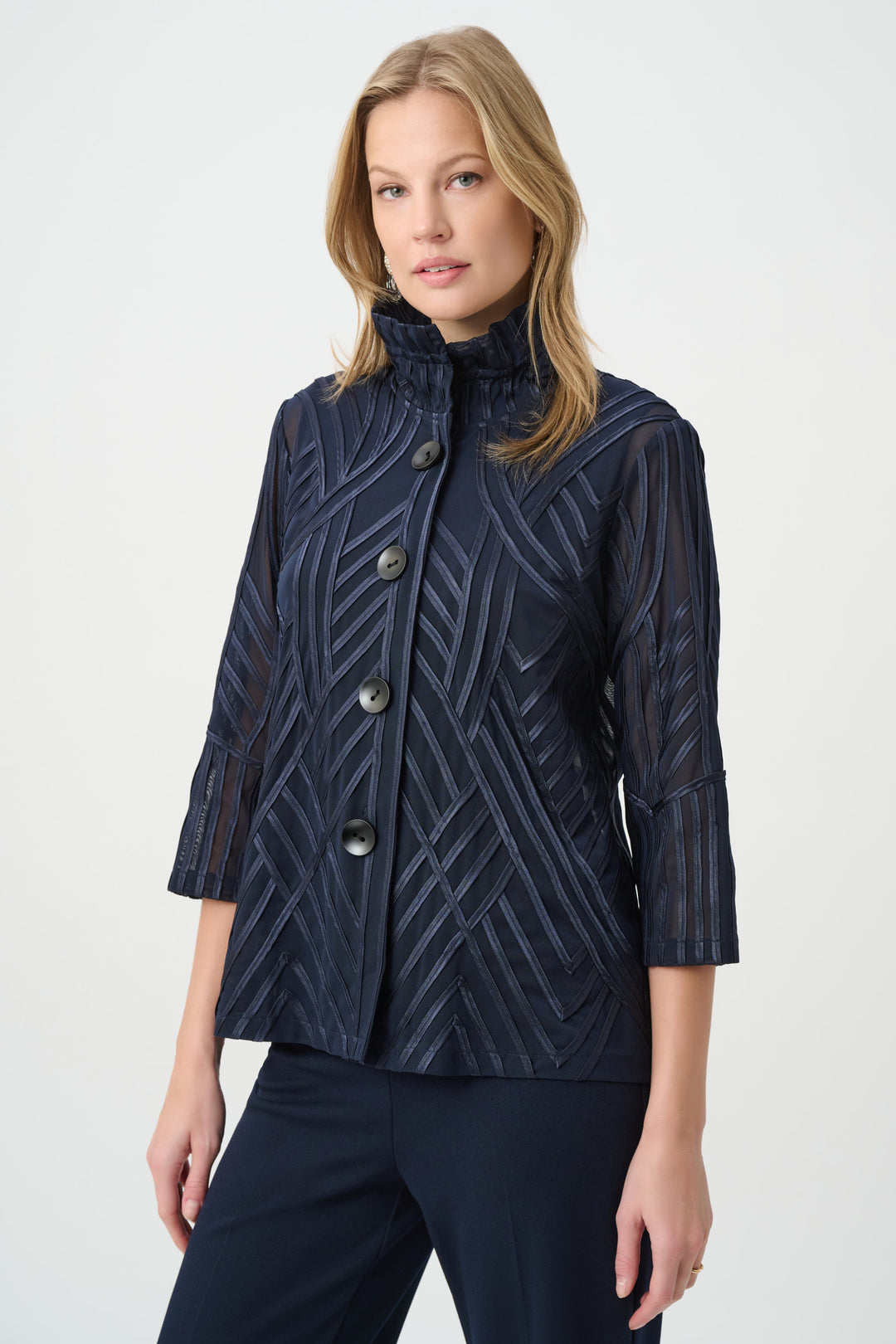 A woman modelling a navy textured jacket with navy pants standing in front of a grey background. 