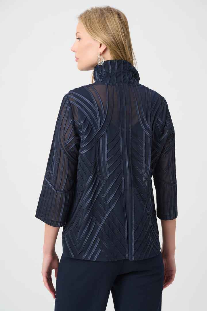 A woman shown from the back modelling a navy textured jacket with navy pants standing in front of a grey background. 